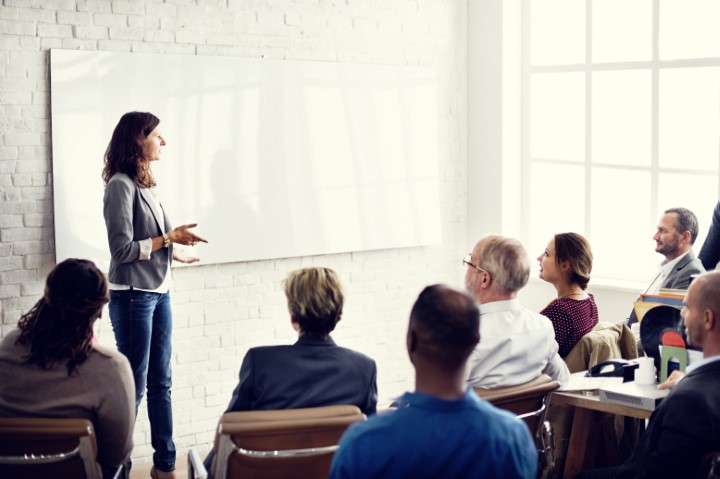 Female teacher gives a lecture to her class in front of a white board